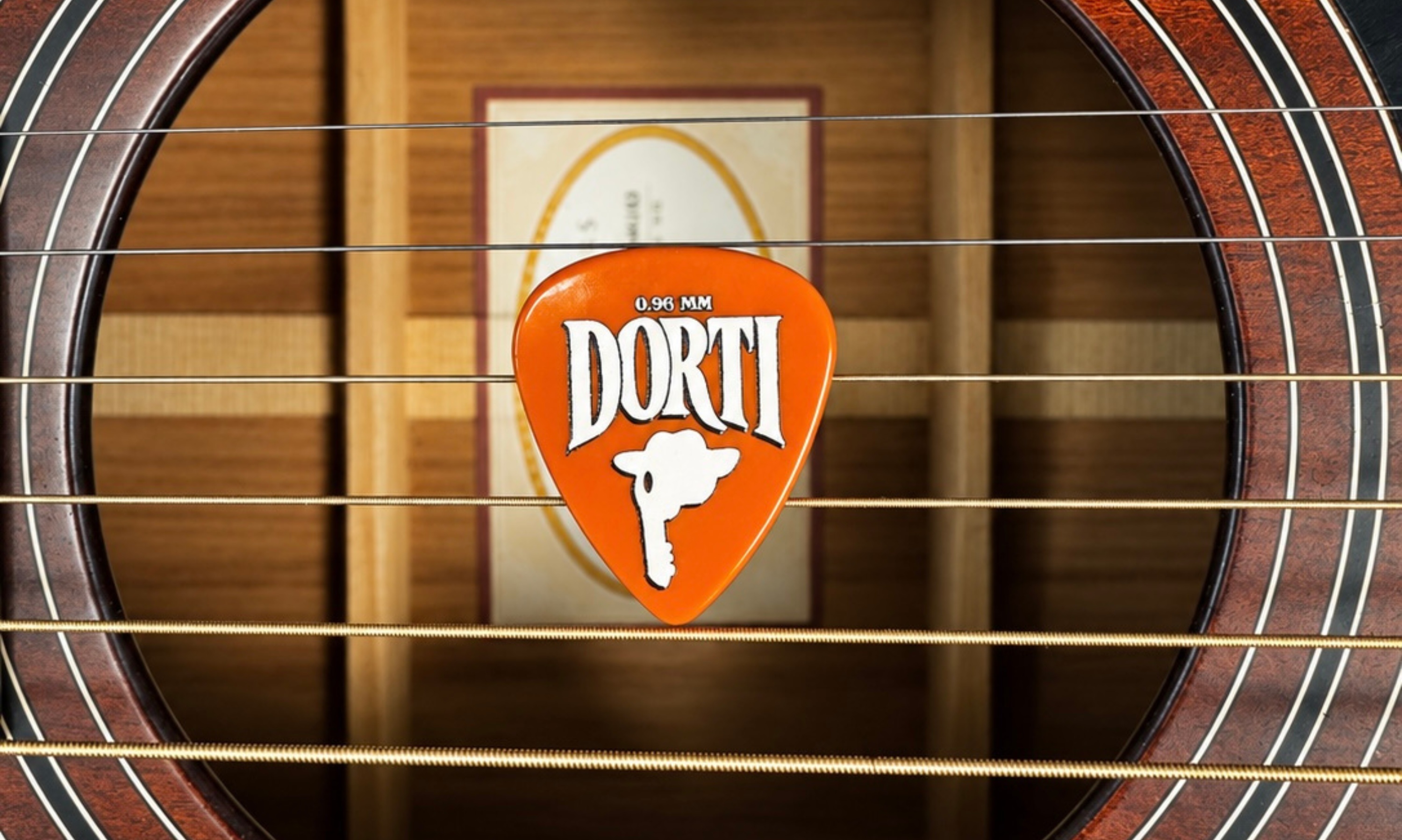 DORTI 0.96mm nylon guitar pick held in the strings over an acoustic guitar sound hole