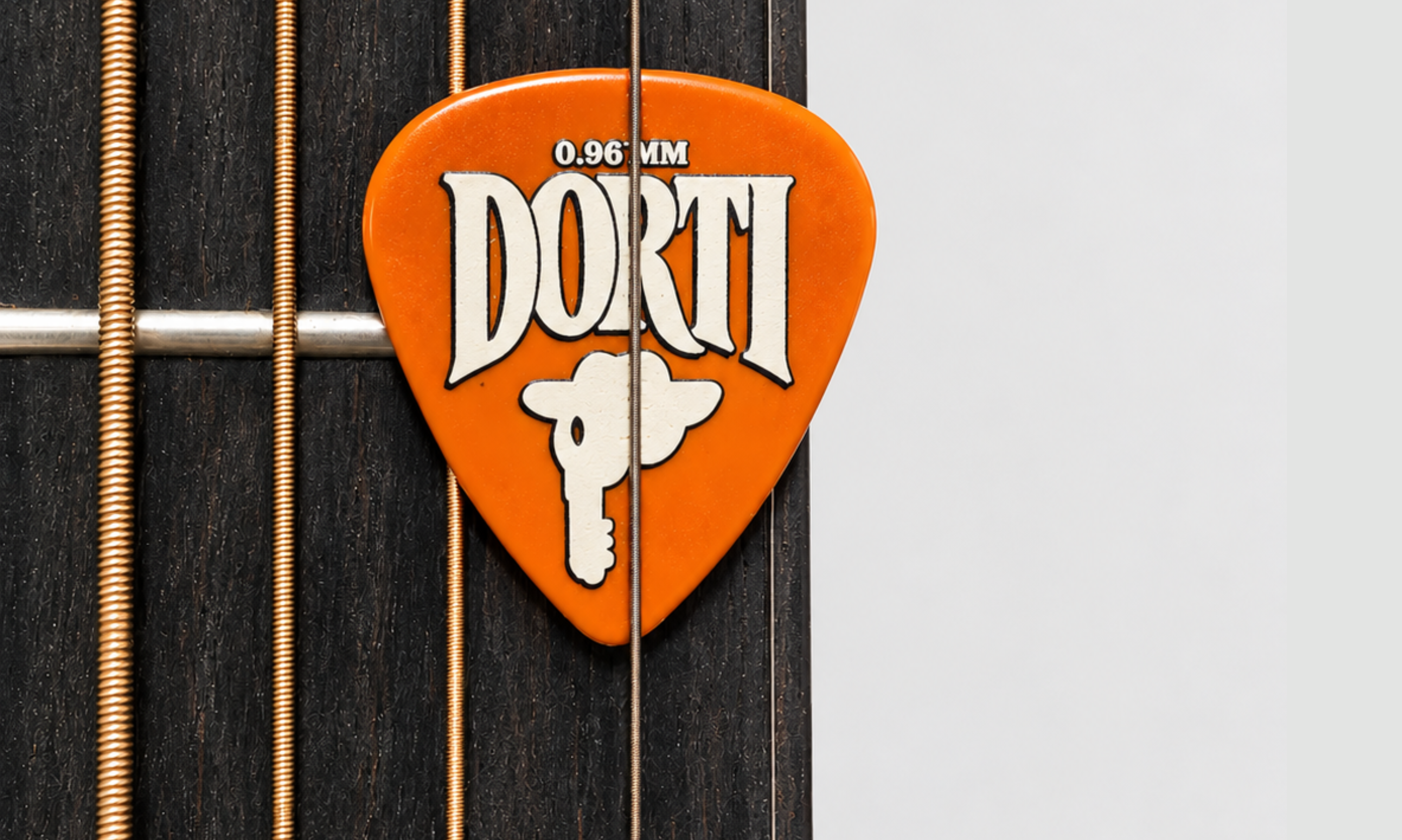 DORTI orange nylon guitar pick resting on the strings over a guitar fretboard