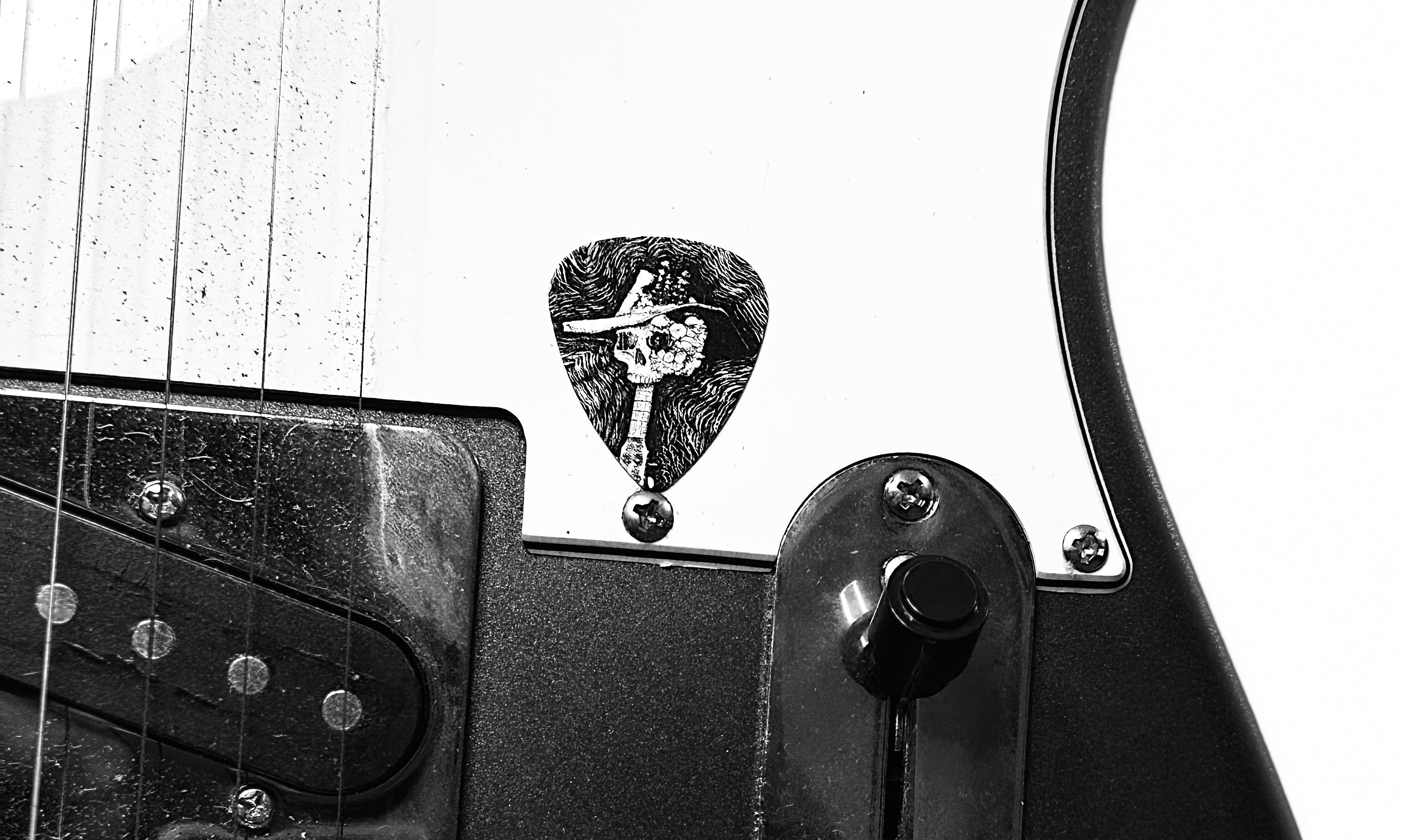 DORTI Jimi Skull steel pick on a black electric guitar, black-and-white photo