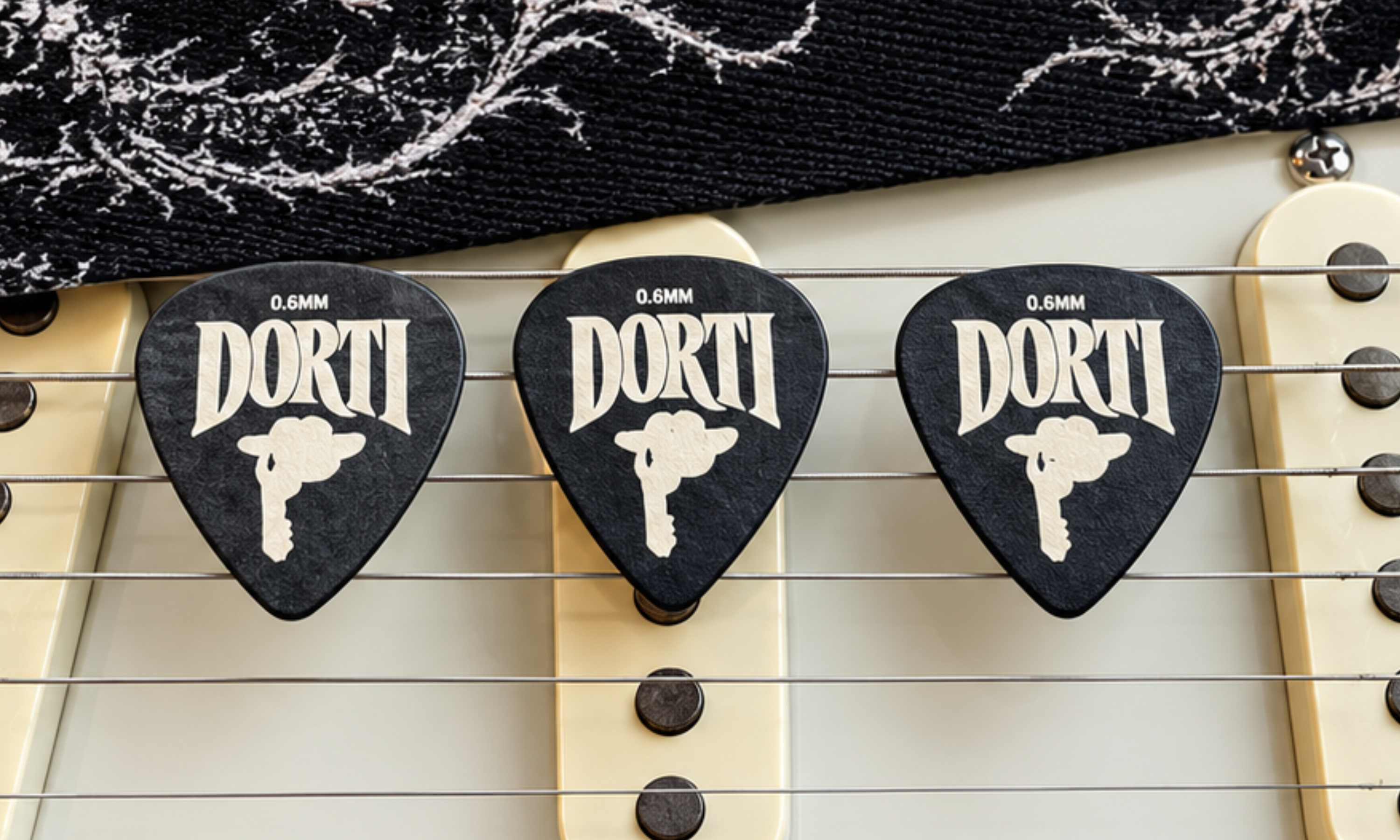 Three black DORTI Delrin guitar picks on the pickups of a white electric guitar
