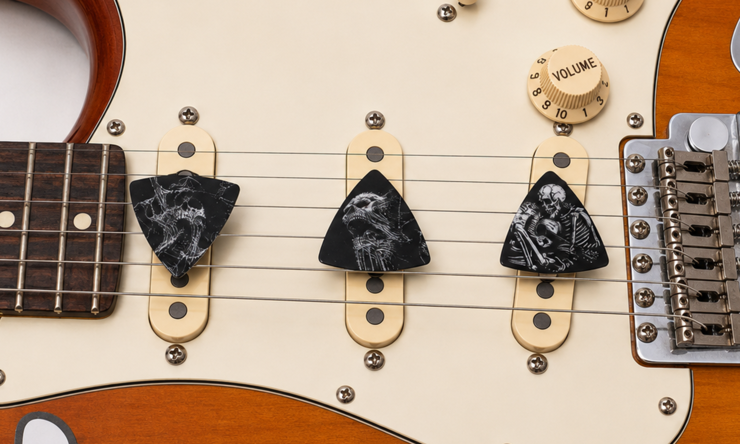 Three DORTI Boneyard Collection guitar picks under the strings of a sunburst electric guitar