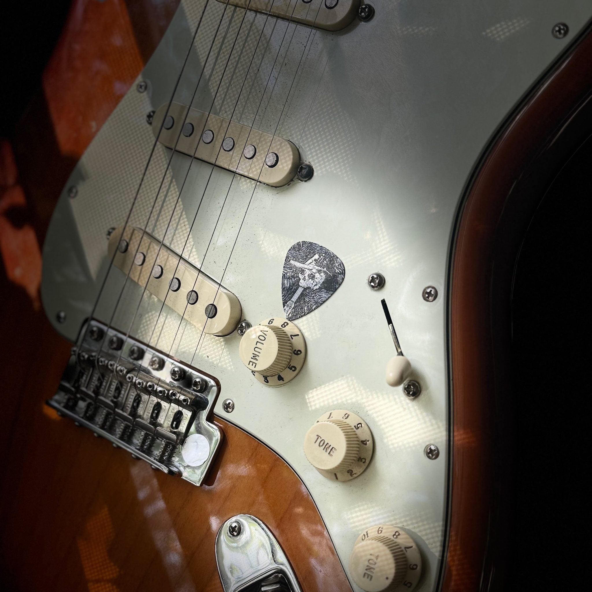 DORTI stainless steel guitar pick on the pickguard of a sunburst Stratocaster