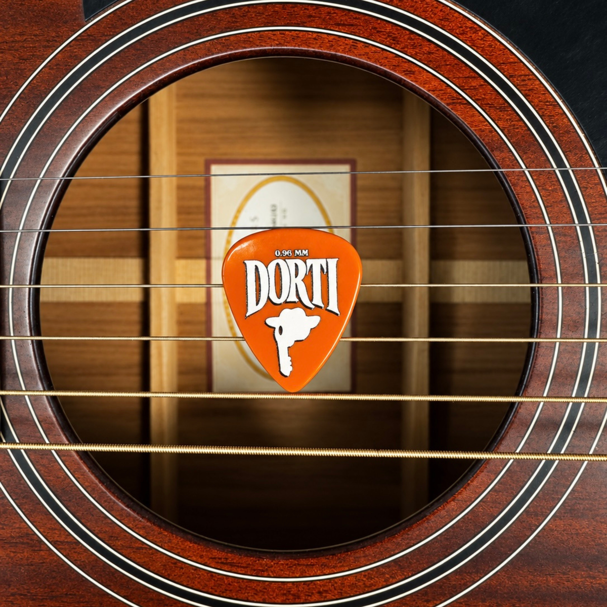DORTI 0.96mm nylon guitar pick held in the strings over an acoustic guitar sound hole