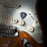 Close-up of a guitar's control knobs and strings featuring the DORTI guitar pick in center frame.