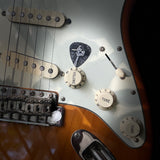 Close-up of a guitar's control knobs and strings featuring the DORTI guitar pick in center frame.