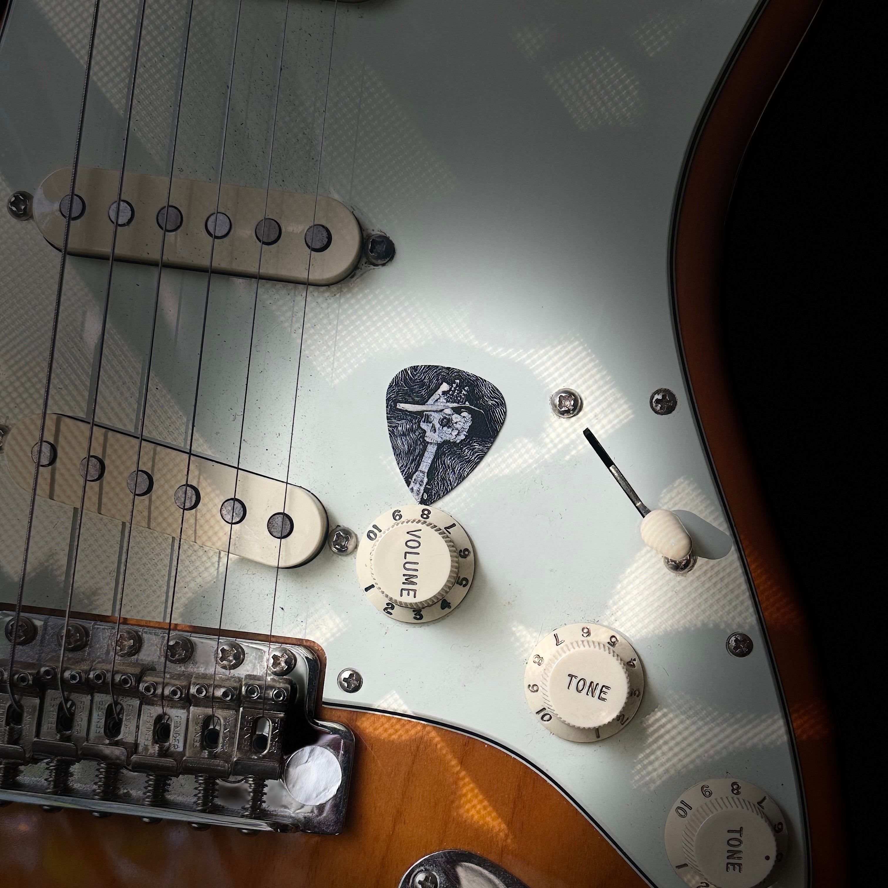 Close-up of a guitar's control knobs and strings featuring the DORTI guitar pick in center frame.