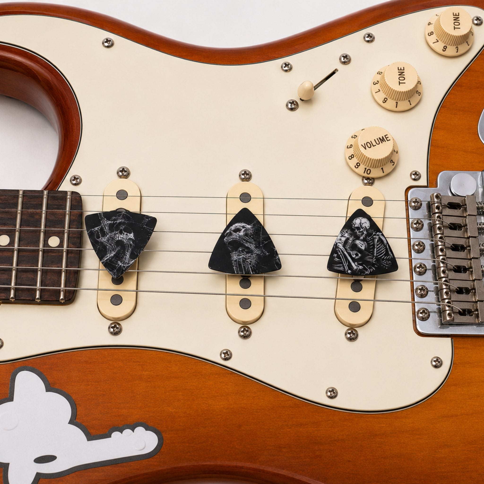 Three DORTI Boneyard Collection guitar picks under the strings of a sunburst electric guitar